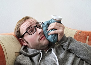 man holding cold compress to his cheek 