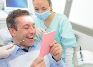 Man in dental chair looking at smile in mirror
